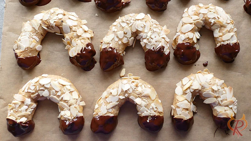 Die Spitzen der gebackenen Mandelhörnchen werden in Zartbitterkuvertüre getaucht